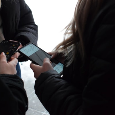 Tre unga tjejer med svarta jackor håller i mobiltelefoner.