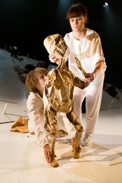 ur kalevalaproduktionen på ÅST: två vitklädda kvinnor håller i en brun dockfigur