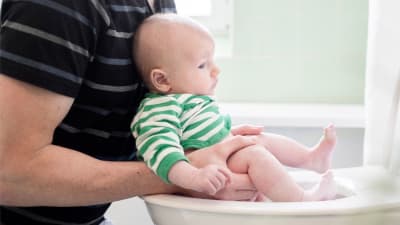En bebis som "grodhålls" ovanför toaletten.