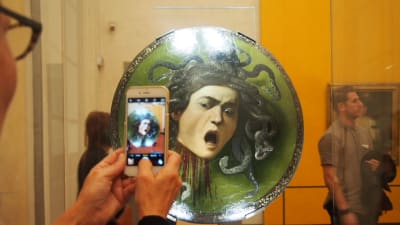 En man fotografer ett konstverk med mobilen på konstmuseet Uffizierna i Florens.