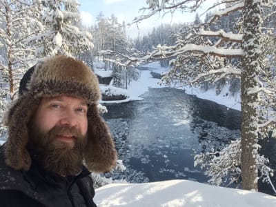 Joakim Lax iklädd pälsmössa i snöigt landskap med liten öppen sjö i bakgrunden.