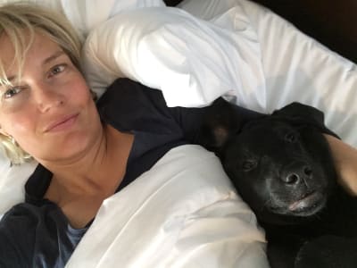 Toimittaja Riikka Suominen köllöttelee sängyssä kainalossaan musta labradorinnoutaja Tepsu.