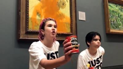 Två unga personer håller upp en tom burk tomatsoppa, vilket de kastat på Vincent van Goghs tavla Solrosor. På deras vita skjortor står: Just stop oil.