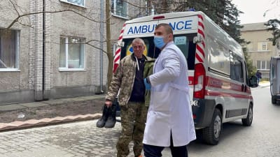 En läkare hjälper en sårad man i camouflagedräkt intill en ambulans.