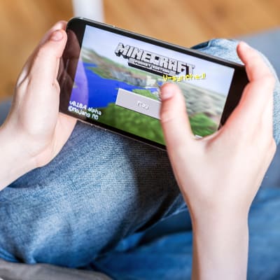 Nuori pelaa Minecraft -peliä puhelimellaan.