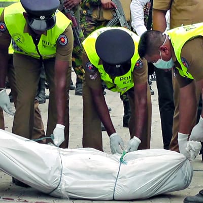 Poliisit siirtävät ruumista valkoisessa muovipussissa pois tapahtumapaikalta Sri Lanka Kalmunaissa.