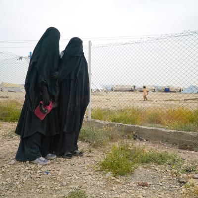 Två kvinnor står framför ett stängsel på lägret al-Hol i Syrien.