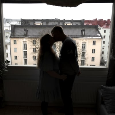 Pariskunta suutelee ikkunan edessä.