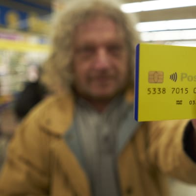 Mies pitää keltaista luottokortin näköistä muovikorttia kameran edessä. Kortissa on siru ja siinä lukee Posteitaliane.