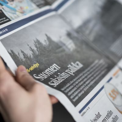En person håller i en Helsingin Sanomat-tidning.