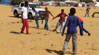 Interna flyktingbarn spelar fotboll, säkerhetsvakt uppe i högra hörnet.