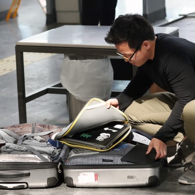 Lentomatkustaja avaa matkalaukkunsa lentokentän turvatarkastuksessa.