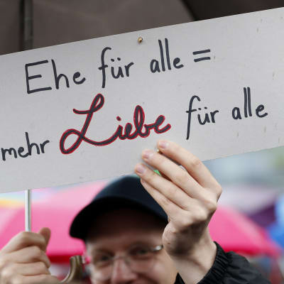 Mies pitelee kylttiä, jossa lukee saksaksi Avioliitto kaikille = Enemmän rakkautta kaikille.