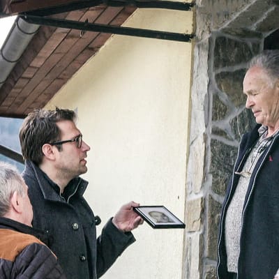 Programledare Niklas Källner visar upp ett foto för en man som står i en dörr.
