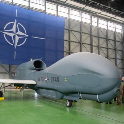 Rq-4d phoenix -drone hangaarissa. Takaseinällä suuri Nato-lippu.