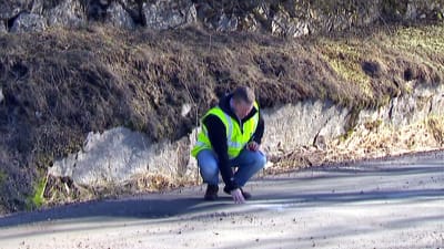 Man på huk inspekterar grusväg.
