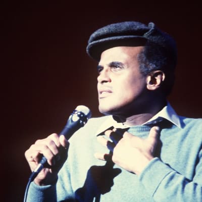 Harry Belafonte laulaa seisten, kohdevalo suunnattu laulajan kasvoille. Miehellä on lyhytlippainen hattu päässä.