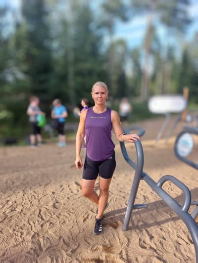 Kvinna står vid gymredskap utomhus.