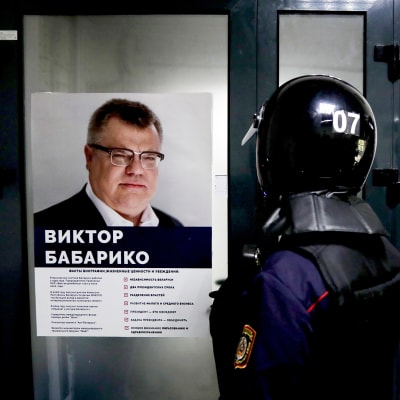Mellakkavarusteisiin pukeutuneet poliisit seisovat Viktor Babarykon kampanjajulisteen edustalla mINSKISSÄ.