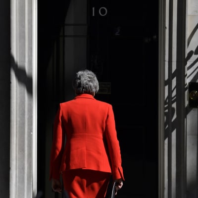 Theresa May kävelee kohti ovea selkä kameraan päin.