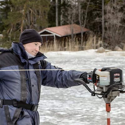Fiskaren Tanja Åkerfelt drar igång isborren på vintern ute på isen en bit från stranden.