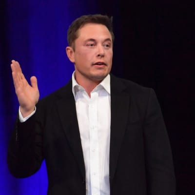 Teslan toimitusjohtaja Elon Musk puhuu, hänen oikea kätensä on viittausasennossa.