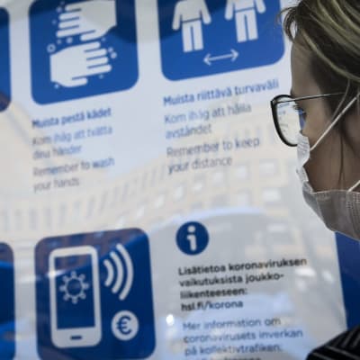 Hengityssuojainta käyttävä nainen katsoi turvallisuusohjeita bussipysäkillä Helsingissä kesäkuussa. 