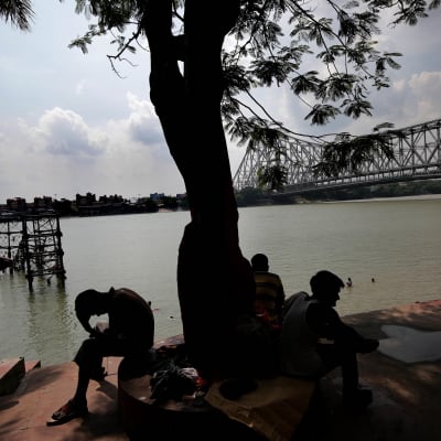 Ihmisiä vilvoittemassa puun alla Ganges-joen rannalla Kolkatassa, Itä-Intiassa.