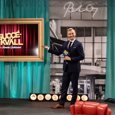 Janne Grönroos står på en scen och pekar på en tavla där det står "Succékväll".