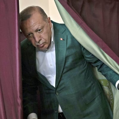 Poliitikko Recep Tayyip Erdogan astuu esiin viininpunaisen verhon takaa.