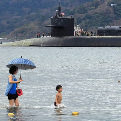 Människor badar på stranden i bakgrunden militärubåten USS Michigan.