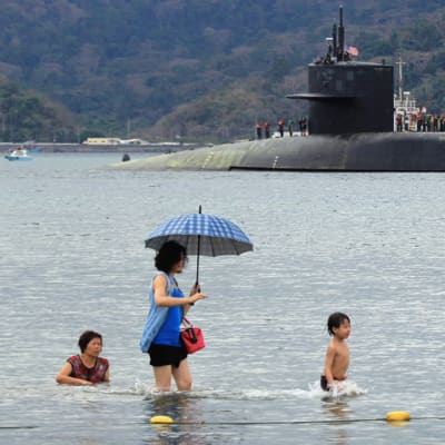 Människor badar på stranden i bakgrunden militärubåten USS Michigan.