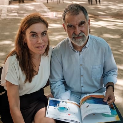 Kuvaa Barcelonan kaduilta. Mies ja nainen istuu puiston penkillä kirja sylissään ja katsoo kameraan. 