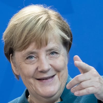 Angela Merkel pekar med pekfingret mot kameran och ler.