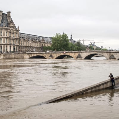 Ihmiset katsovat kohti Louvren museota puoliksi veden varaan peittyneen tien varrella Seinen rannalla.
