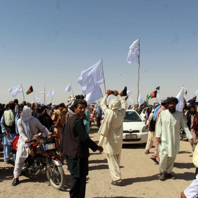 Talibanin taistelijoita saapumassa Afganistanin Kandahariin juhlimaan paatokauden päättymistä. Ihmisjoukko aukiolla käsissään valkeita lippuja ja Afganistanin lippuja.