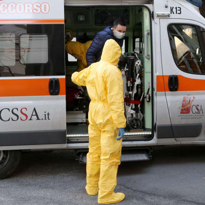 Suojapukuihin pukeutuneet terveystyöntekijät auttavat henkilöä ulos ambulanssista Italian Paduassa.