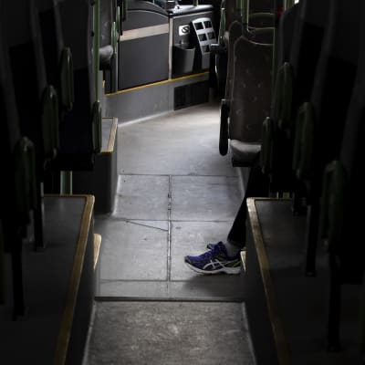 Matkustajan jalat tyhjällä bussin käytävällä.