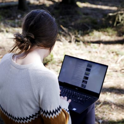 Kuvassa nainen tekee etätöitä tietokoneella metsässä.