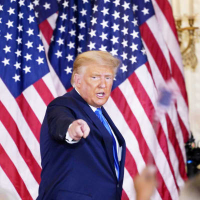 Yhdysvaltain presidentti Donald Trump osoittaa kameraa, taustalla Yhdysvaltain lippuja