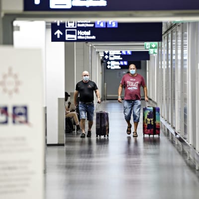 Kaksi matkustajaa kävelee matkatavaroidensa kanssa Helsinki-Vantaan lentoasemalla.