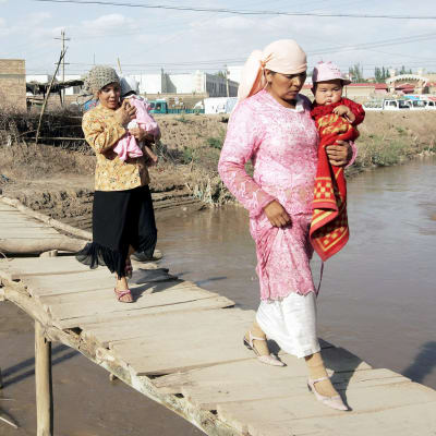 Kaksi uiguurinaista kantaa lapsia sillalla.