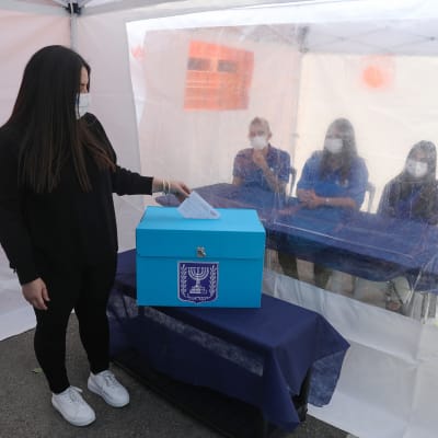 Israelilainen nainen äänestää ja ääntentarkkailijat tarkkailee äänestämistä muovin takaa.