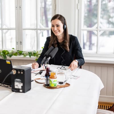 Sanna Marin håller distansmöte vid ett bord i Villa Bjälbo. Framför henne står några flaskor saft.