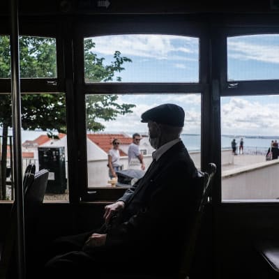 Vanhempi henkilö istuu raitiotievaunussa ja ikunoista näkyy Lissabonin maisemia.