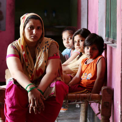 Kavita Gautam istuu roosan värisessä huoneessa kolmen lapsensa kanssa.