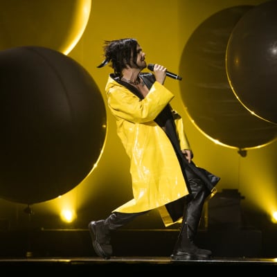 En man i gul regnrock sjunger på en scen. Bakgrunden är svart.