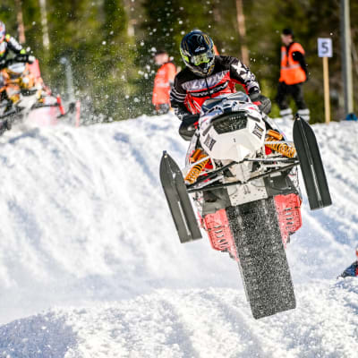 Moottorikelkkakilpailujen voittaja ajaa kelkalla vauhdikkaasti lumisessa maastossa.