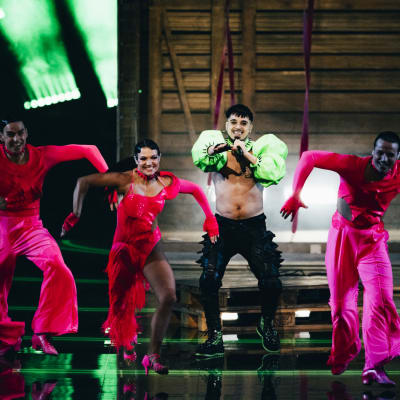 Käärijä iklädd grön bolero står och dansar med sina fyra dansare klädda i ljusröda kläder.