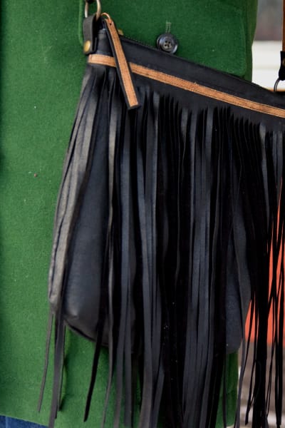 En svart läderhandväska med fransar som hänger mot en grön yllekappa.